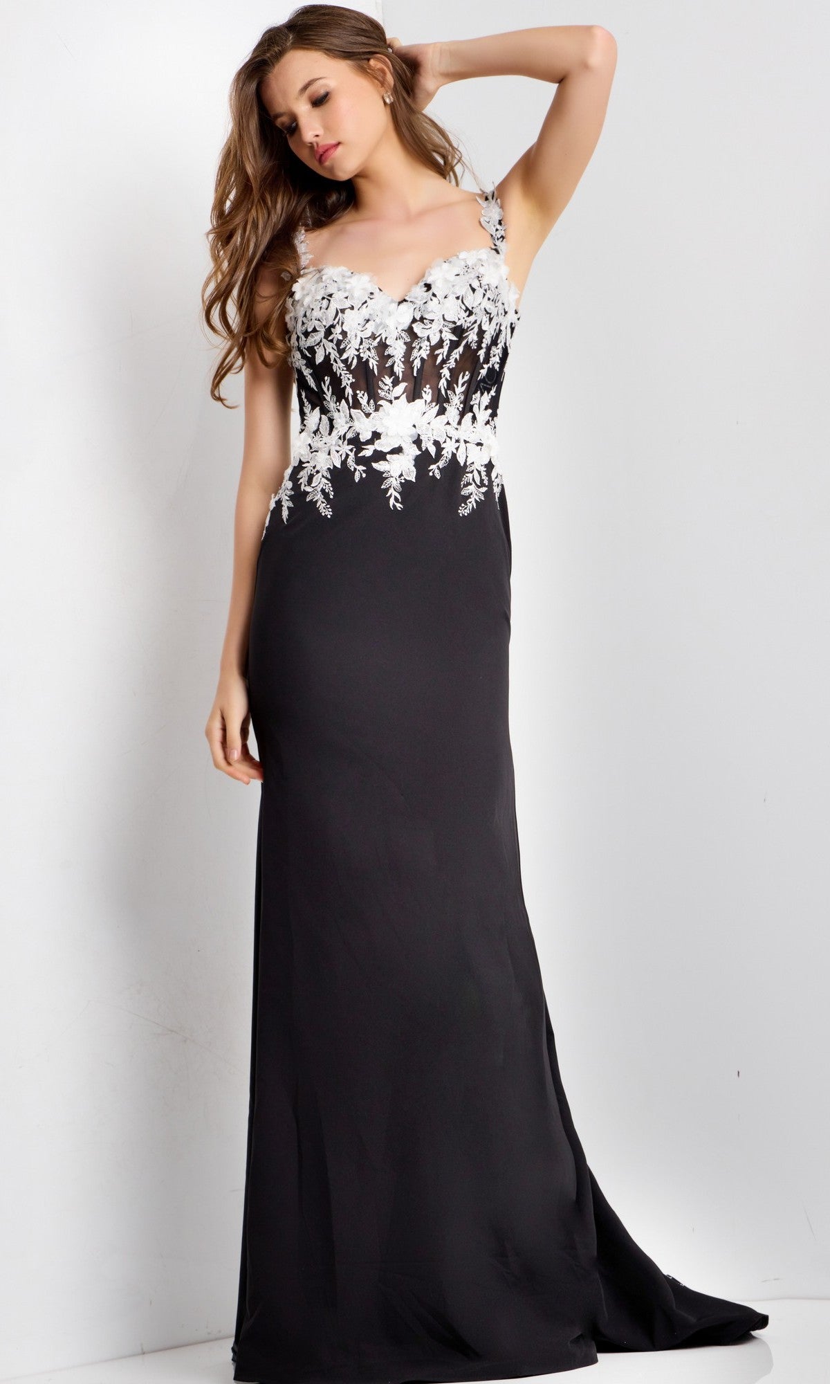 A woman stands against a plain light background wearing the Jovani 49465 long prom dress, which features a sleeveless bodice with white 3D floral appliques and lace detailing, and a black floor-length skirt.